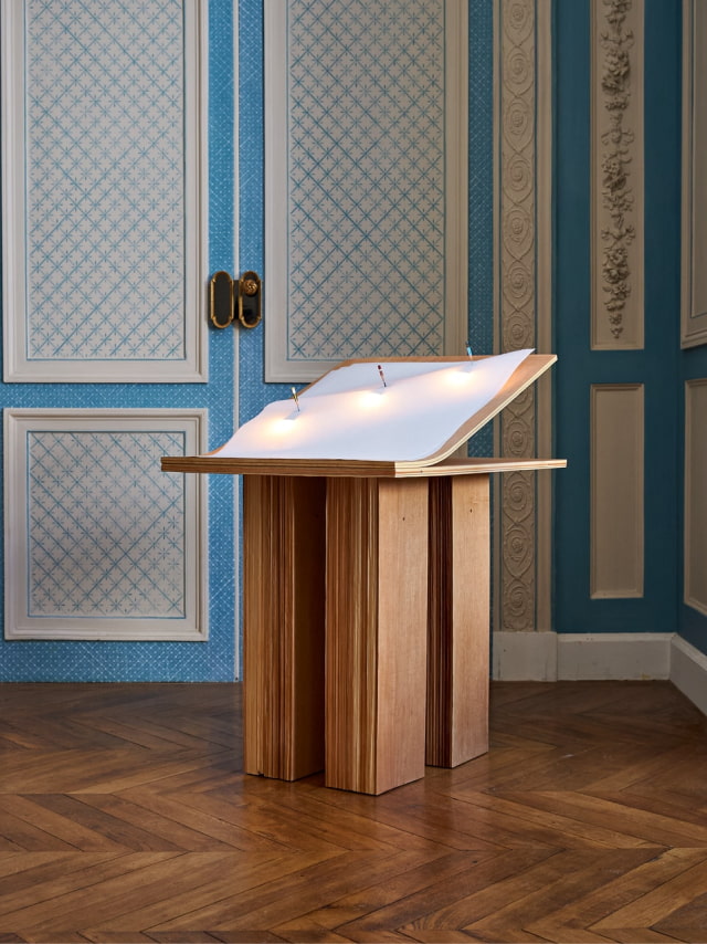 New Form by Yoonjeong Lee, a wooden table and lamp with a paper lampshade held by pencils.